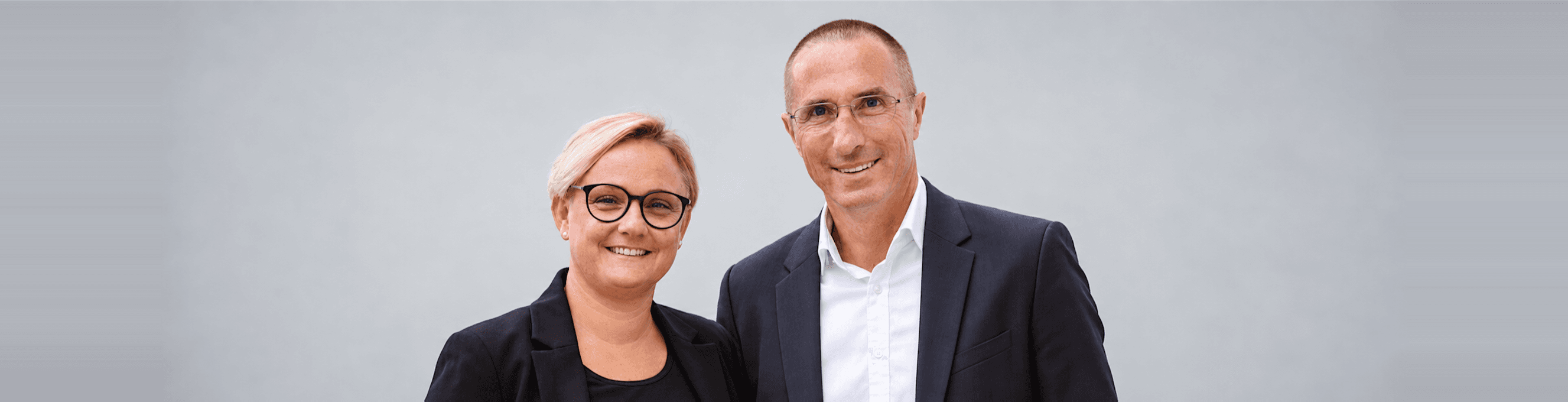 Hermine und Norbert Brigelhuber von SIMMOMAKLER vor grauem Hintergrund
